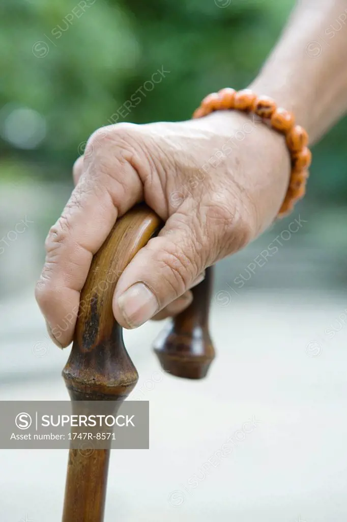 Elderly man holding cane, close-up of hand