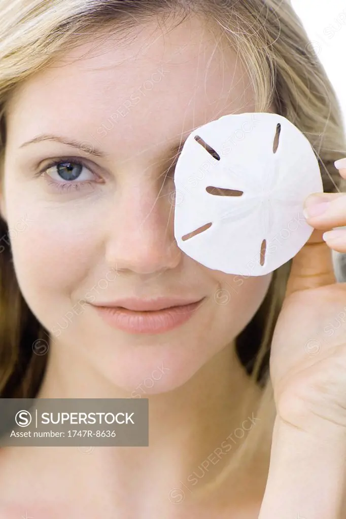 Woman covering one eye with sand dollar, smiling at camera, portrait