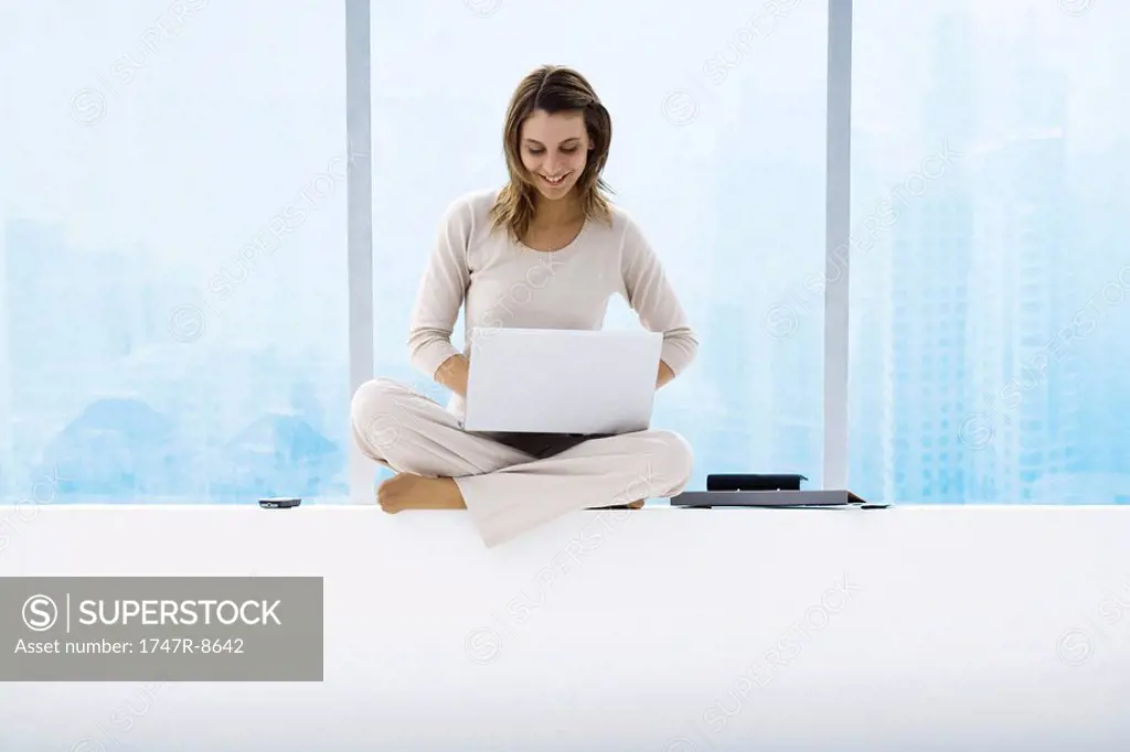 Woman sitting on windowsill using laptop, high rises in background