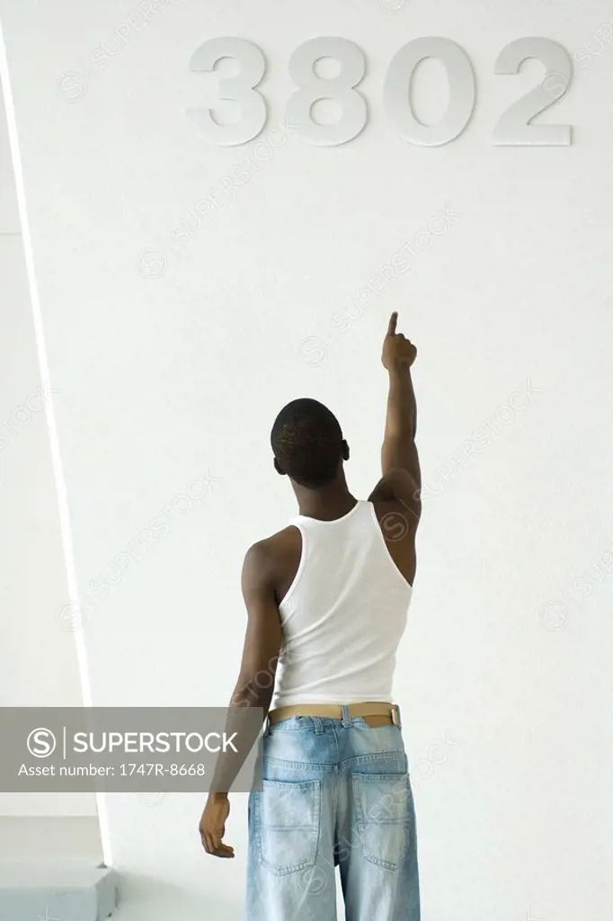 Teenage boy pointing at numbers on wall, rear view