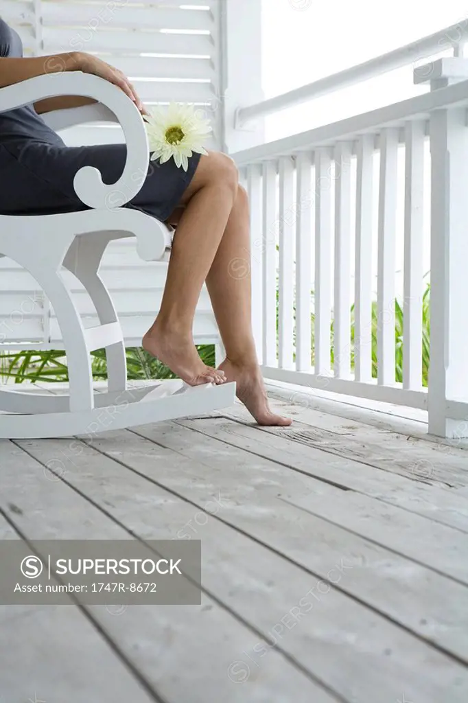 Woman sitting in rocking chair on porch, holding flower on lap, cropped view