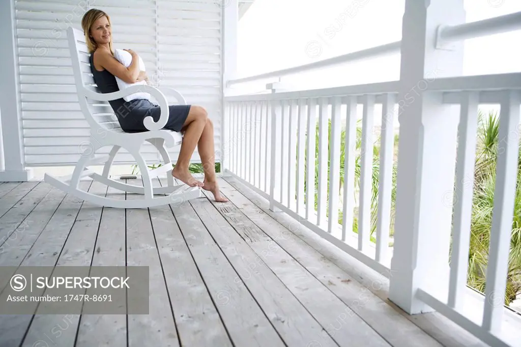 Woman sitting in rocking chair on porch, hugging pillow, looking away