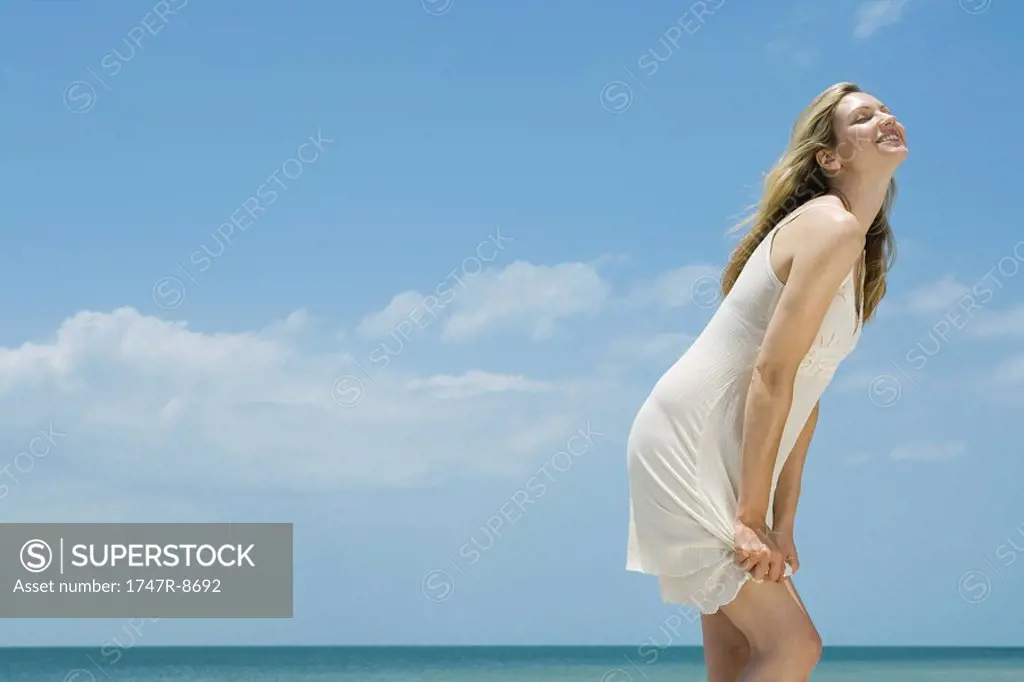 Young woman in sundress standing by the sea, head back, eyes closed, side view