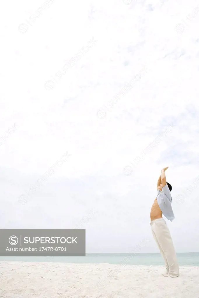 Man standing in sun salutation pose on beach, side view