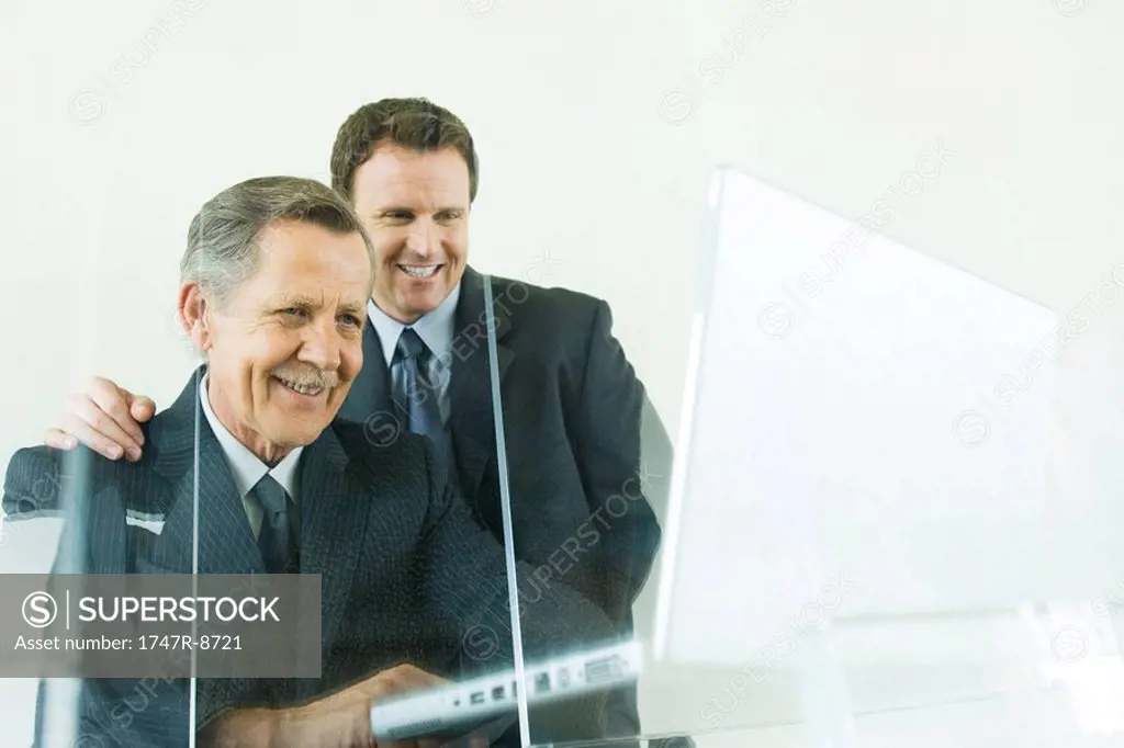 Businessman looking over colleague´s shoulder at laptop computer, both smiling, low angle view