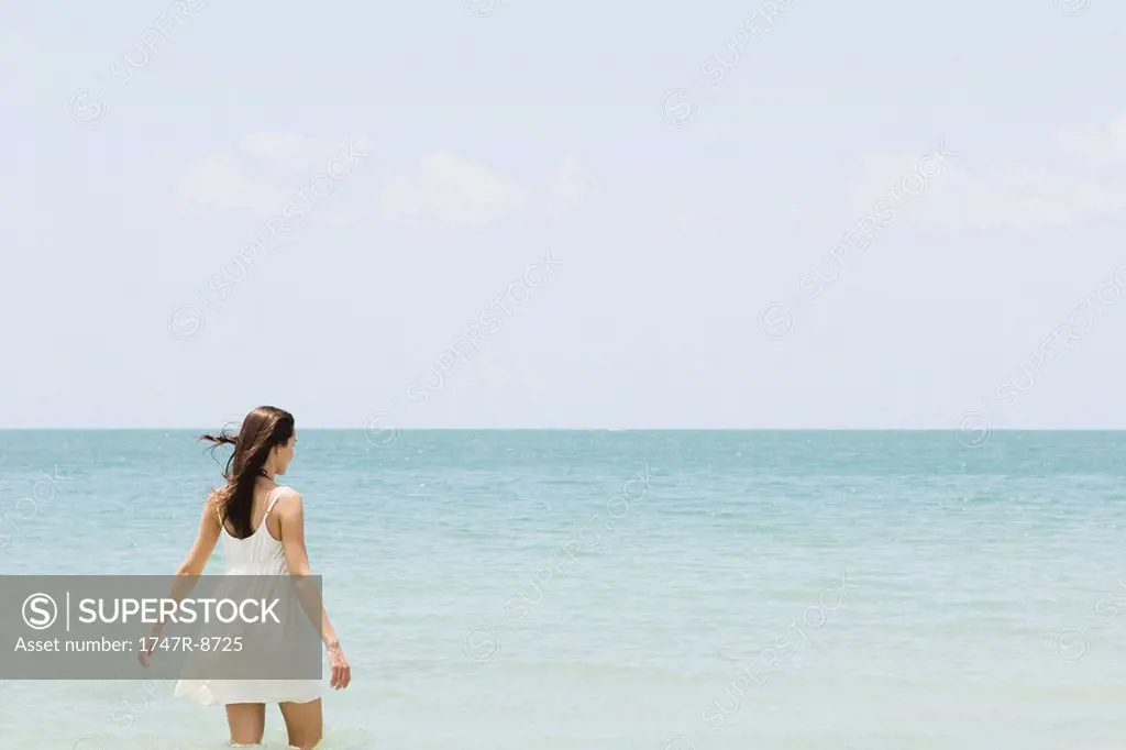 Young woman in sundress standing knee deep in ocean, rear view