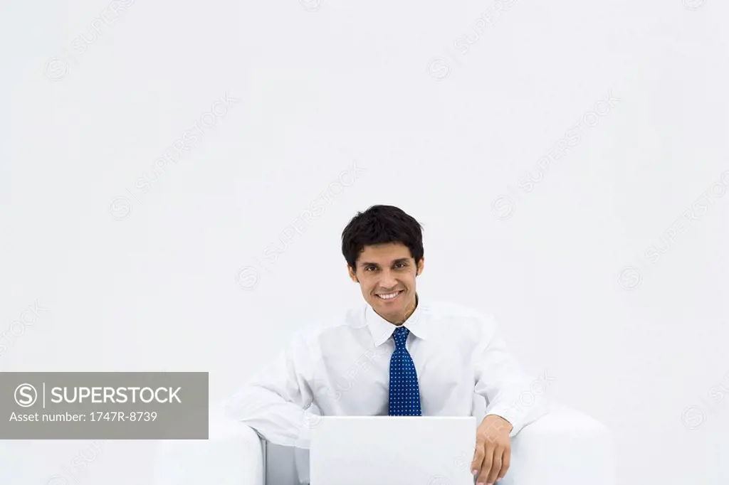Businessman sitting on armchair using laptop, smiling at camera
