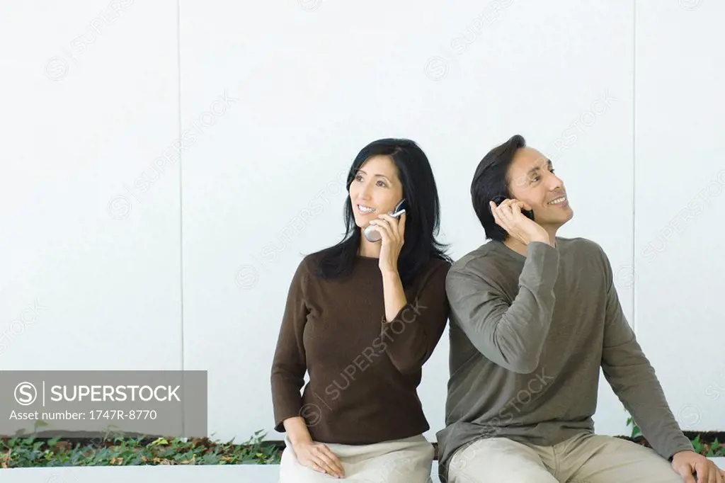 Couple sitting side by side, both using cell phones