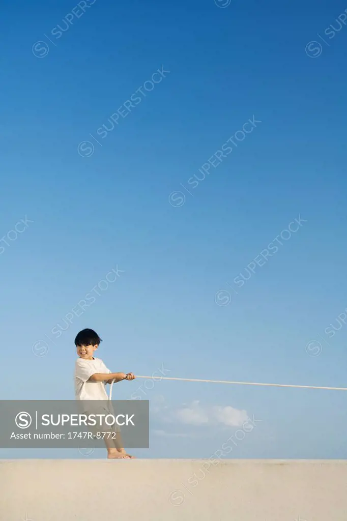 Little boy playing tug-of-war, smiling at camera, mid-distance
