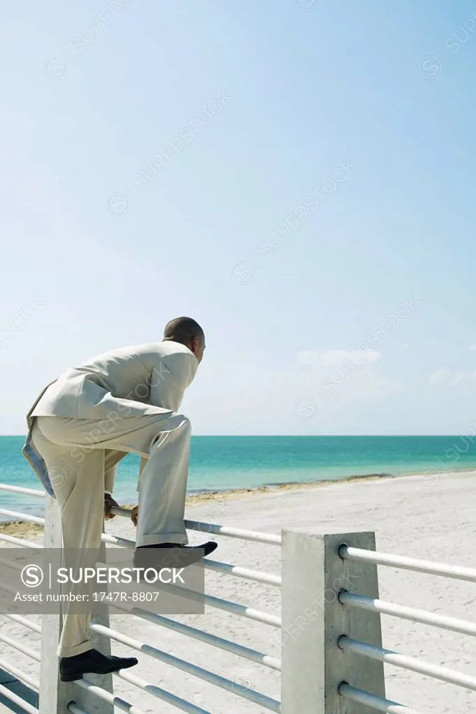 Businessman climbing over fence at the beach, side view