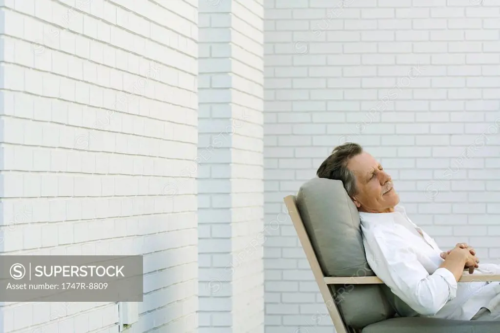 Senior man sitting in chair with eyes closed, side view
