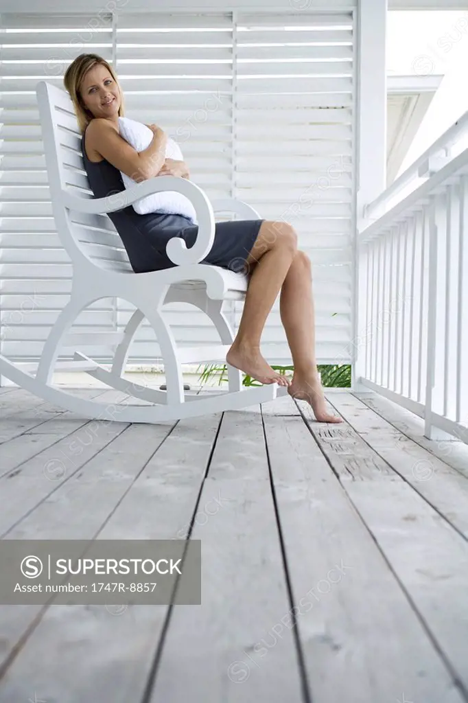 Woman sitting in rocking chair on porch, hugging pillow, smiling at camera