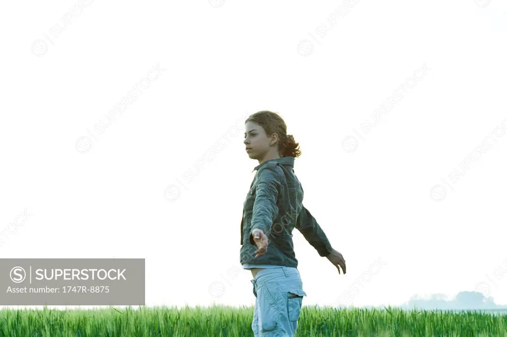 Teenage girl standing with arms out in field, looking away