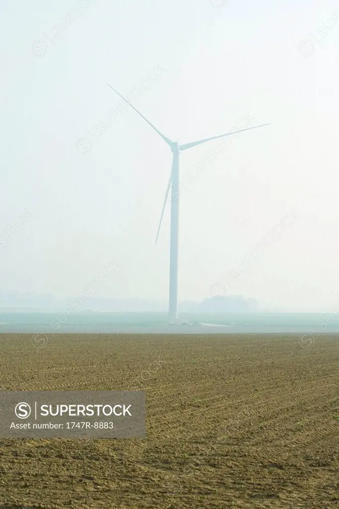 Wind turbine in plowed field, foggy background