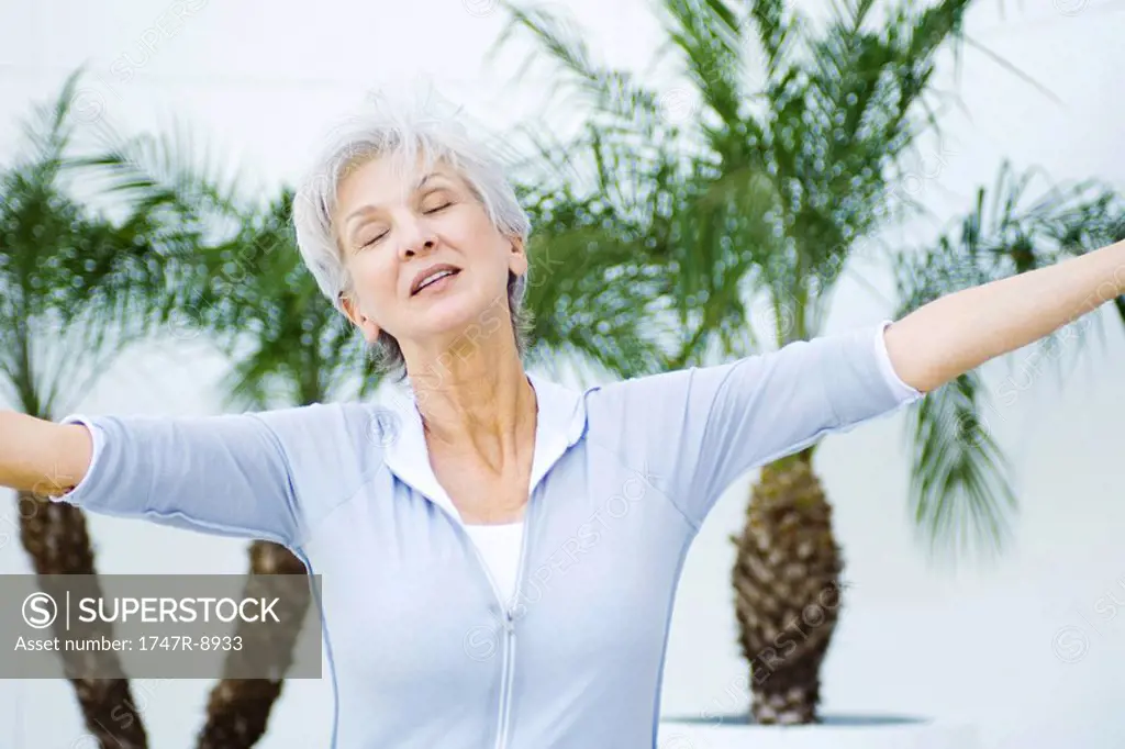 Senior woman with arms outstretched, head tilted, eyes closed