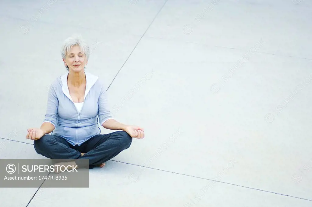 Senior woman sitting in lotus position on the ground, eyes closed