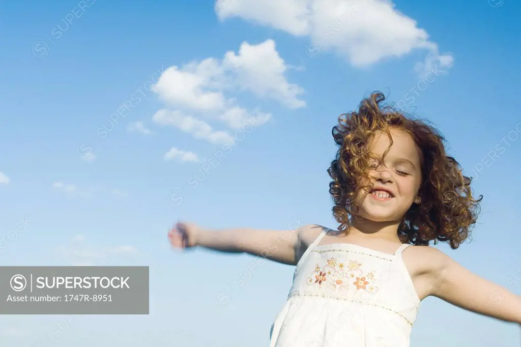 Young girl jumping in the air, arms outstretched, eyes closed, waist up