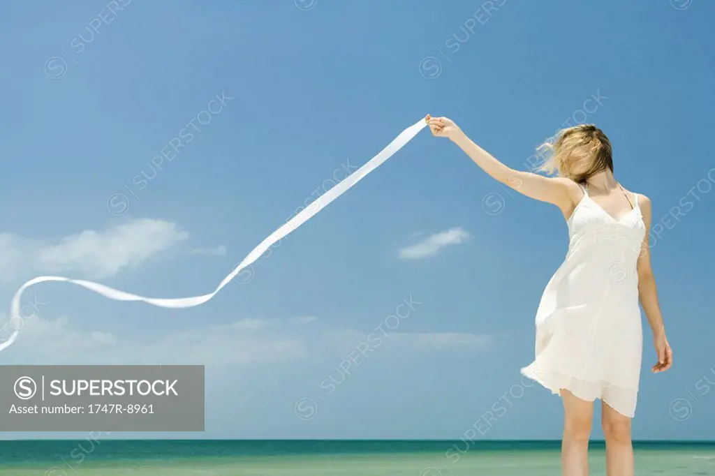 Woman in sundress holding up ribbon in breeze, hair covering face