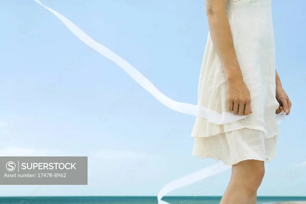 Woman in dress holding ribbon, tousled by wind, low angle view, cropped