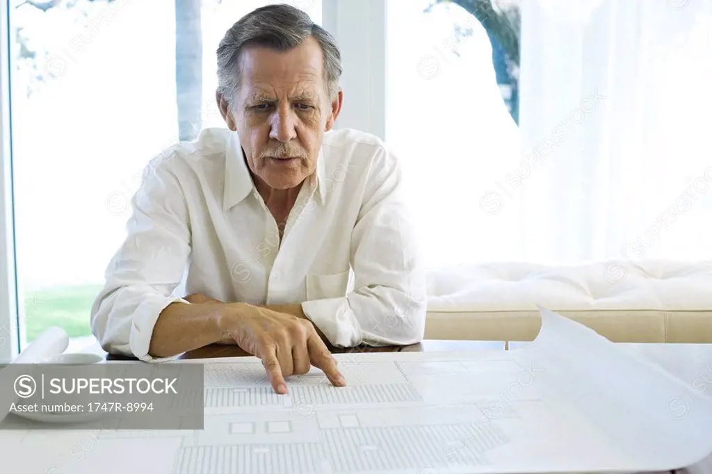 Man studying blueprints in home, cup of coffee nearby