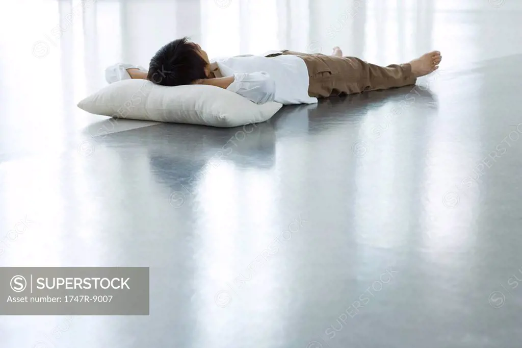 Man lying on floor with head on pillow, full length