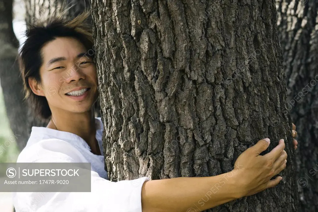 Man hugging tree trunk, smiling at camera