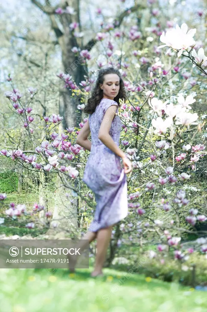Young woman in dress walking in meadow, looking over shoulder, low angle view