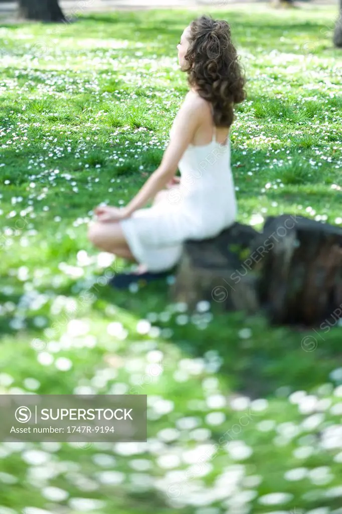 Young woman sitting in lotus position in meadow, side view, selective focus
