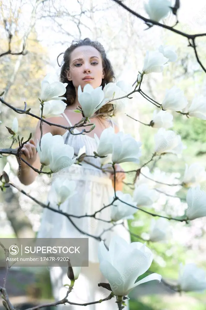 Young woman standing among flowering tree, looking at camera