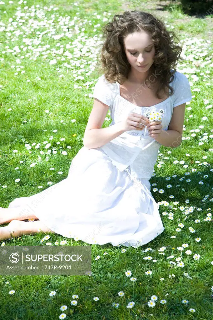 Young woman sitting in meadow, holding flowers, high angle view
