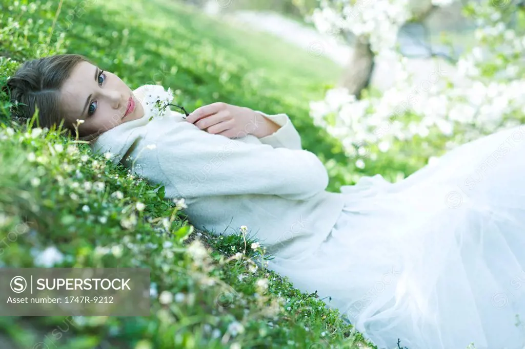 Teenage girl lying on the ground, holding flowers, looking at camera