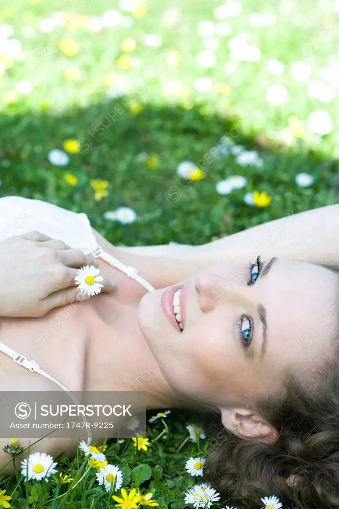 Young woman lying in grass, holding flower, smiling at camera