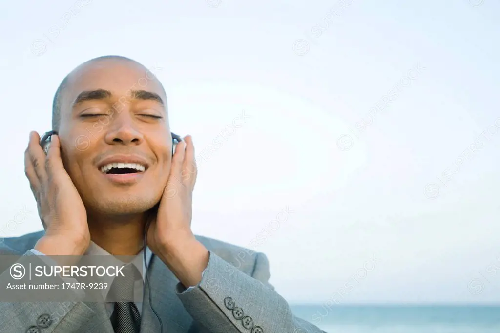 Businessman listening to headphones outdoors, smiling, eyes closed