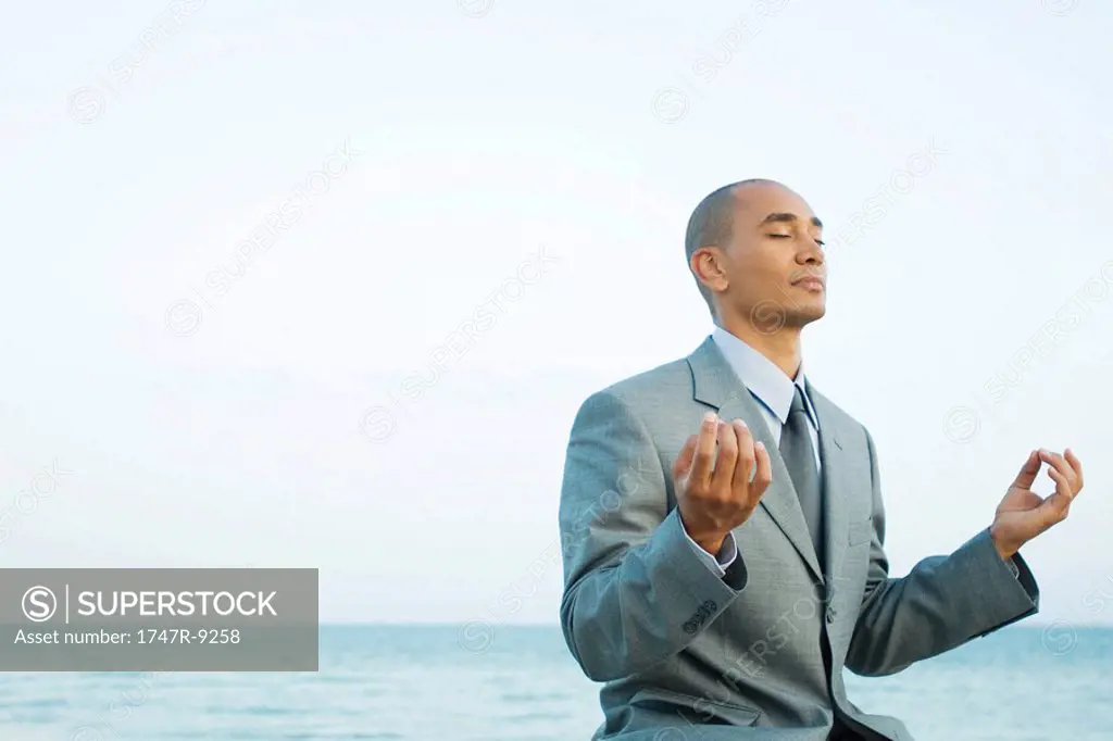 Businessman sitting by the sea in lotus position, eyes closed