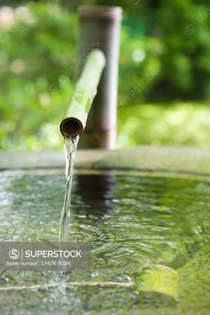 Water flowing from bamboo spigot into basin, close-up
