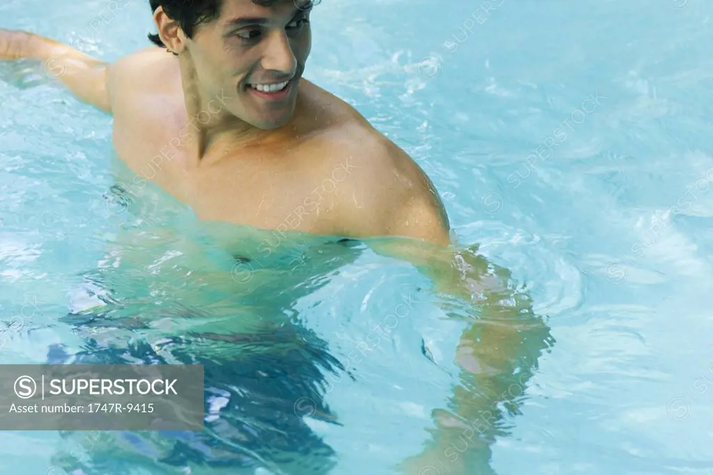 Man standing in swimming pool, looking over shoulder, smiling