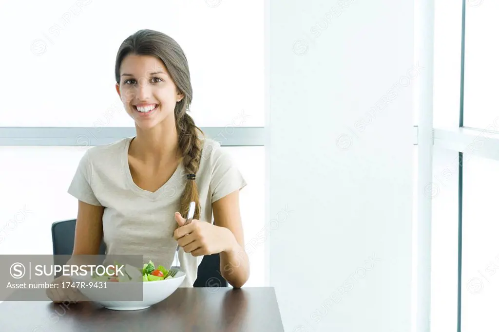 Teen girl eating salad, smiling at camera