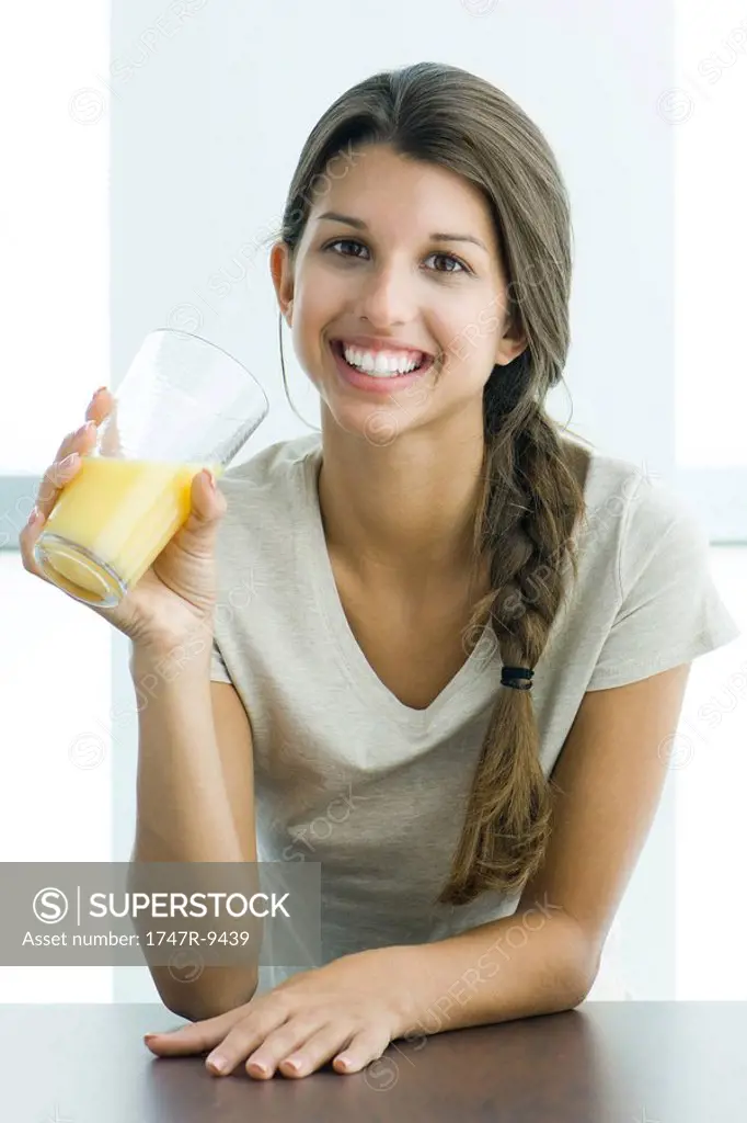 Teen girl drinking glass of orange juice, smiling at camera