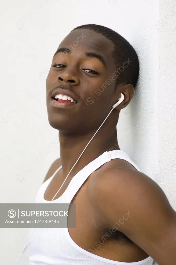 Teen boy listening to earphones, looking at camera, portrait