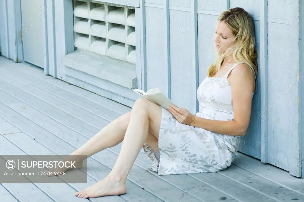 Young woman sitting on deck, reading book