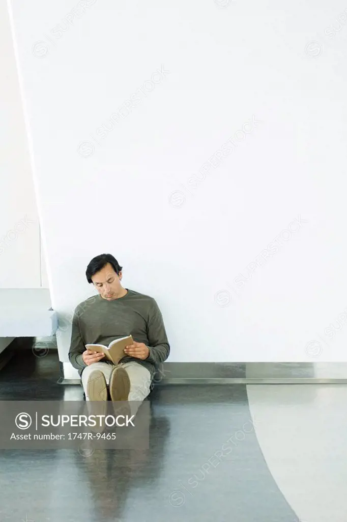 Man sitting on floor, reading book, full length