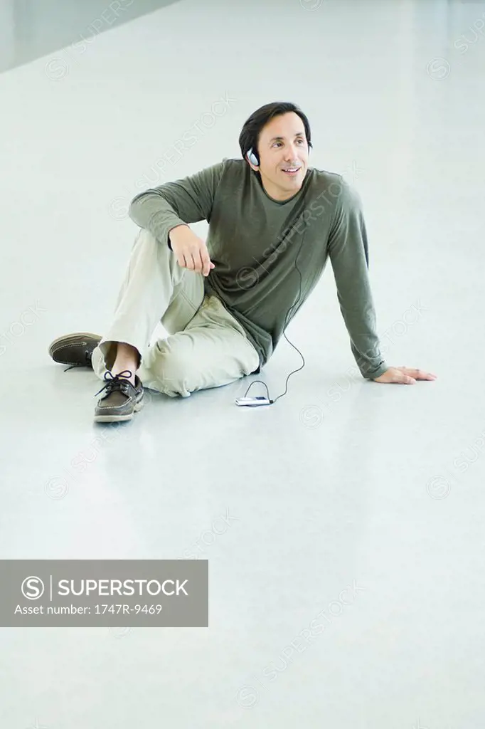 Mature man sitting on floor, listening to MP3 player, full length