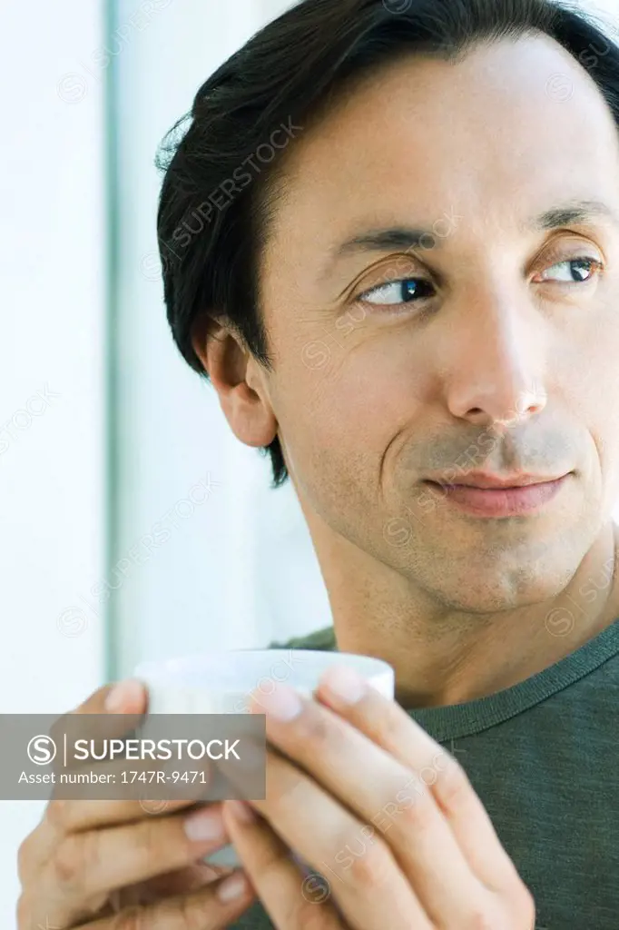 Mature man holding up cup, looking away, smiling