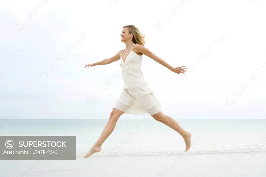 Woman jumping at the beach, arms out, side view