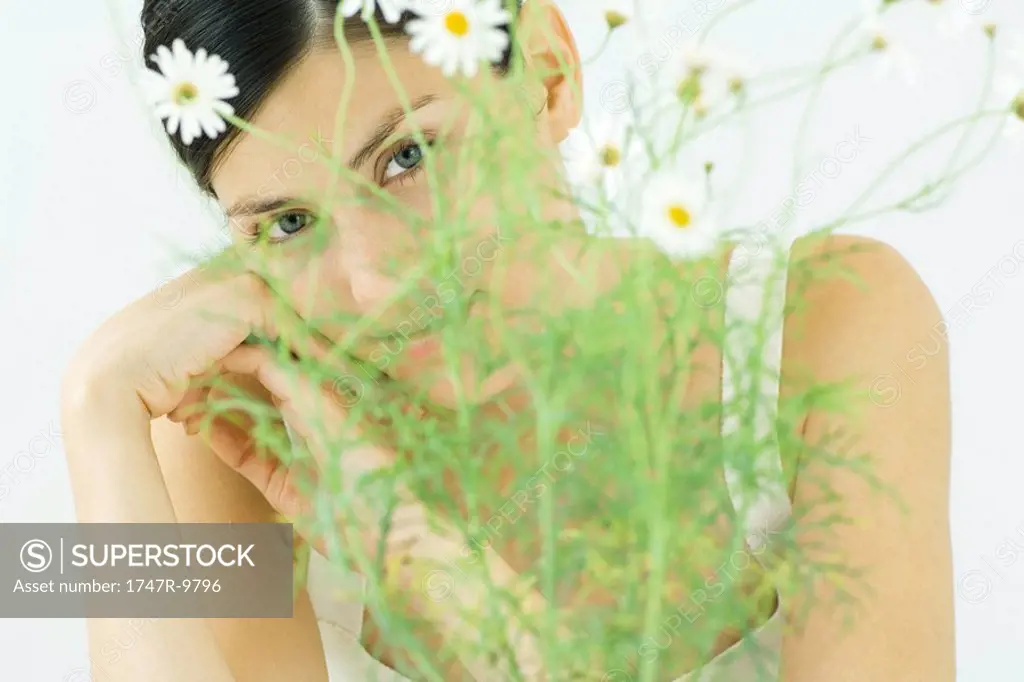 Woman behind chamomile plant, looking at camera, close-up