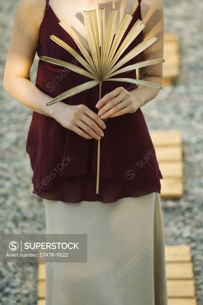 Woman holding dried palm leaf, cropped view