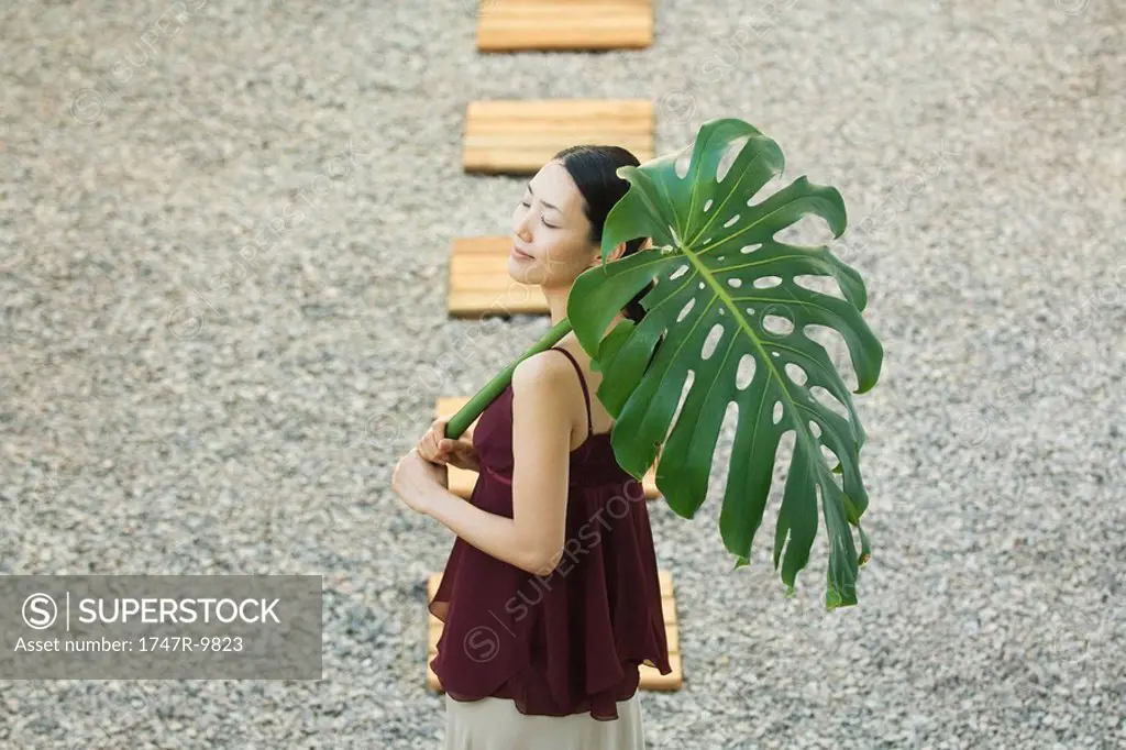 Woman on footpath holding palm leaf, eyes closed, high angle view