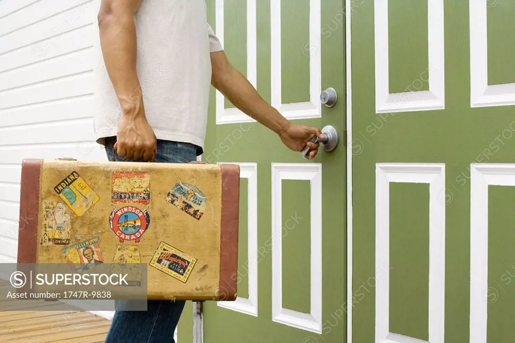 Male traveler carrying suitcase, opening door, cropped view