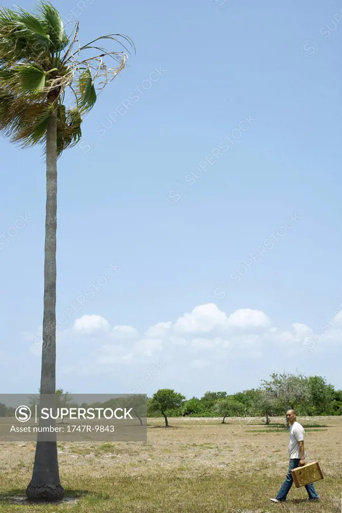 Man walking in tropical landscape, carrying suitcase