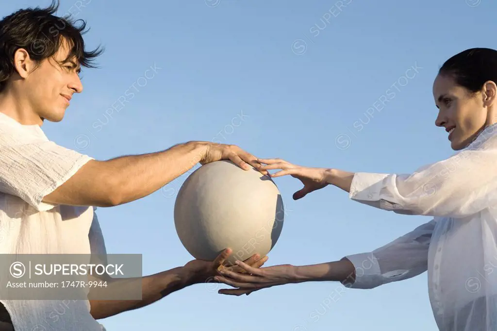 Couple standing face to face, man passing ball to woman, low angle view